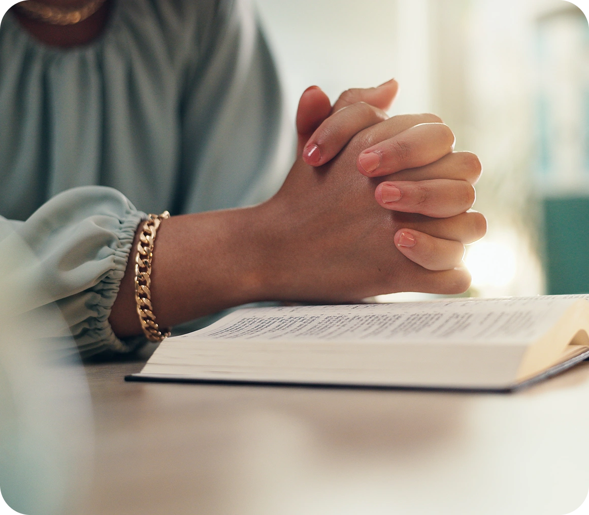 Person praying with hands clasped over an open book indoors.